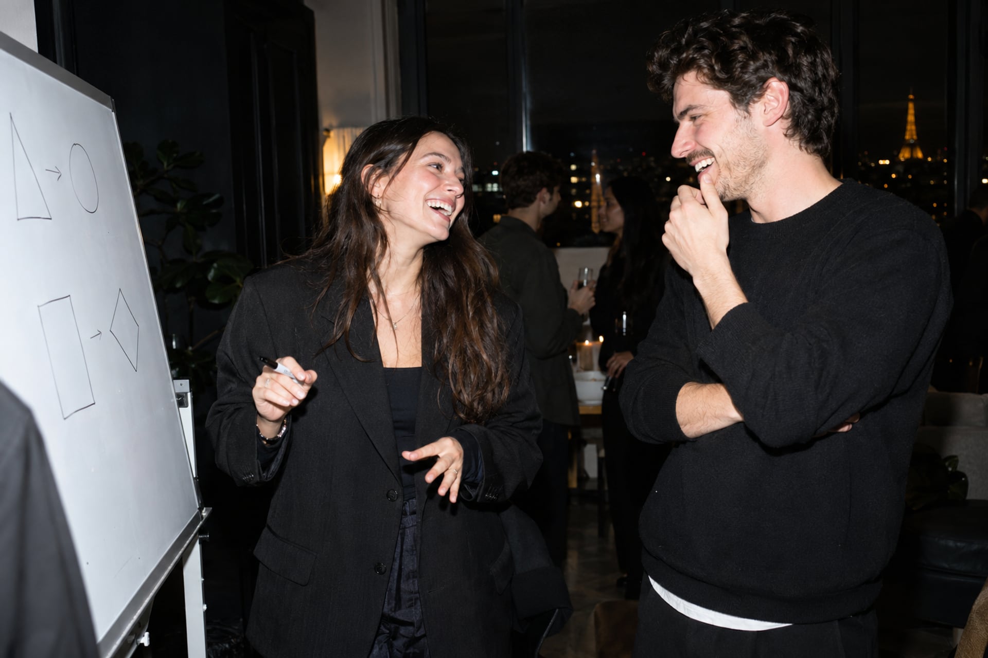 Founders share a laugh beside a Paris meetup whiteboard.