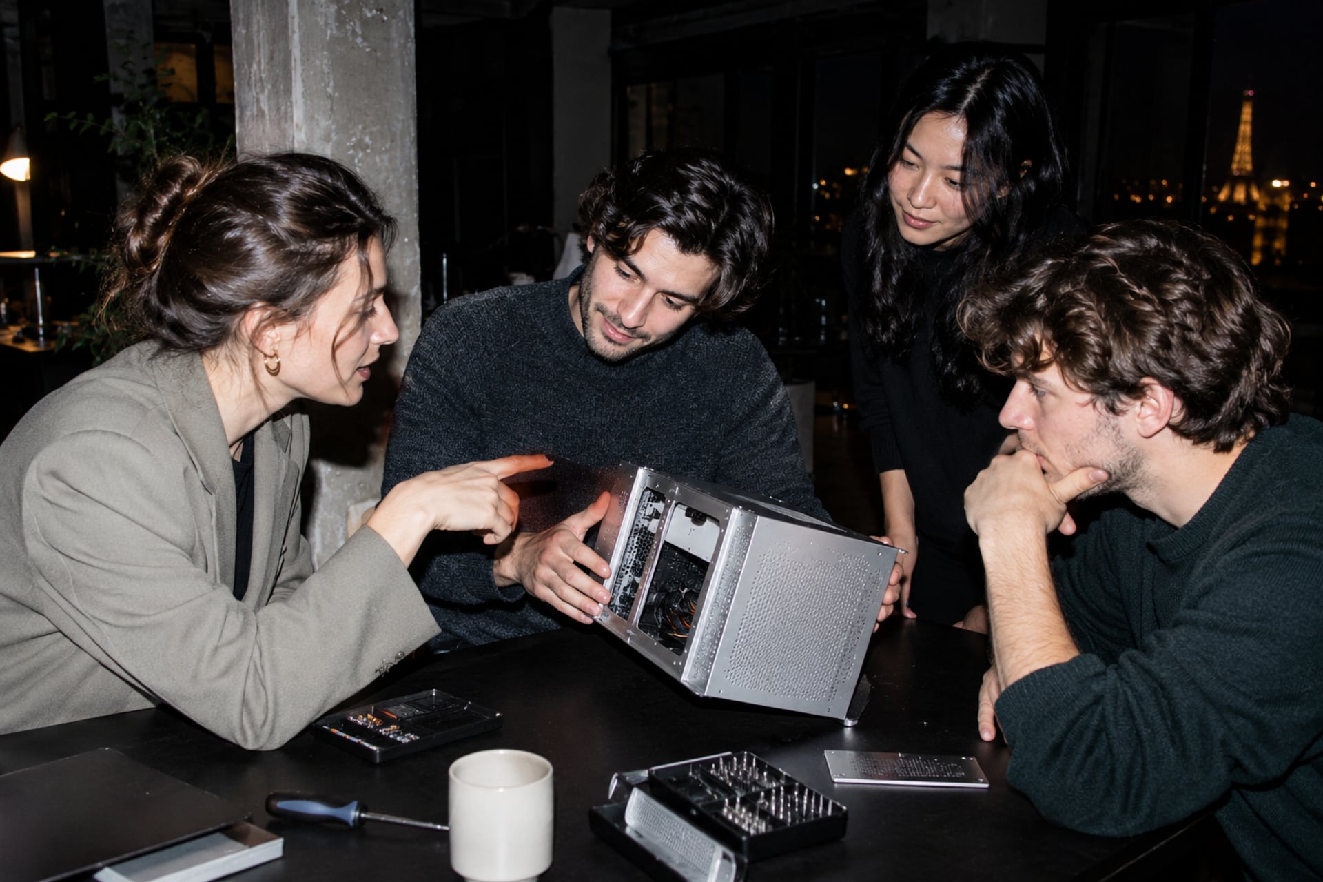 Engineering friends discuss a computer prototype in a Paris loft after dark.